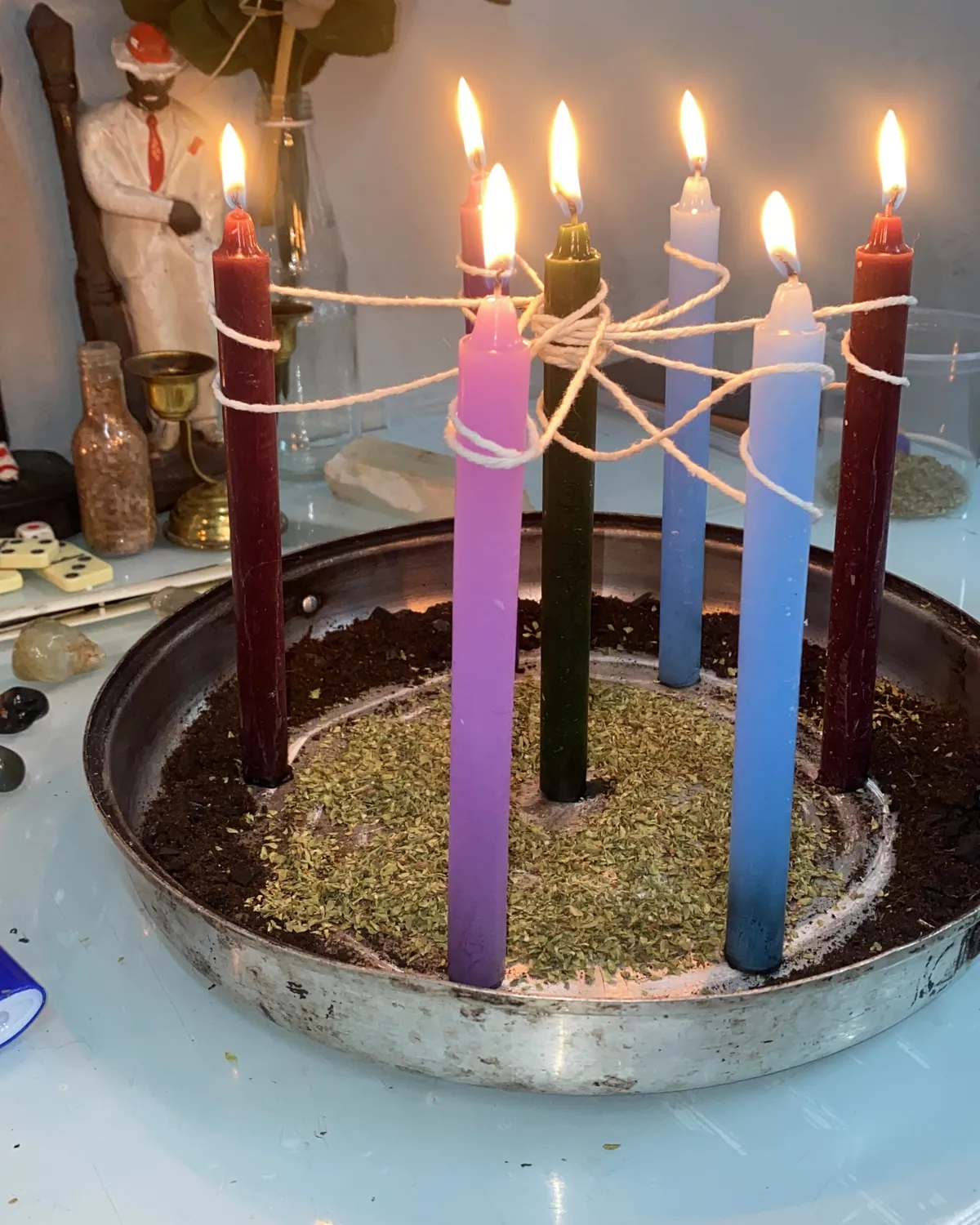 Velas coloridas amarradas umas às outras por fios, sobre uma bandeja com ervas, em ritual de corte de laços