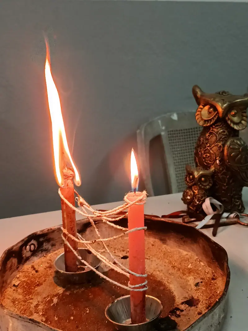 Velas vermelhas amarradas por fio branco, uma delas acesa, sobre bandeja de cobre