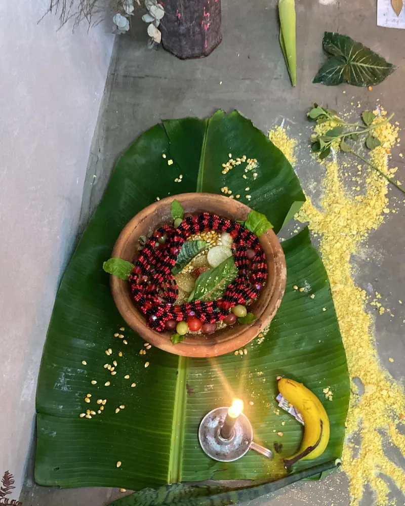 Oferenda sobre folha de bananeira com tigela de sementes, banana e vela acesa